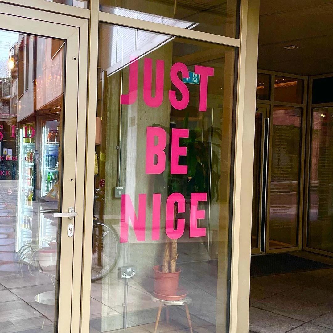 Picture of a glass wall with the words JUST BE NICE painted on it.